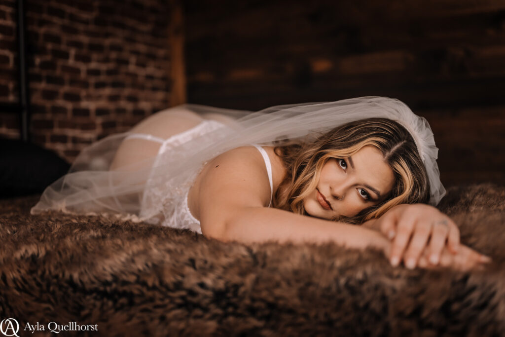 Bride in lingerie lying on brown fur in moody boudoir lighting